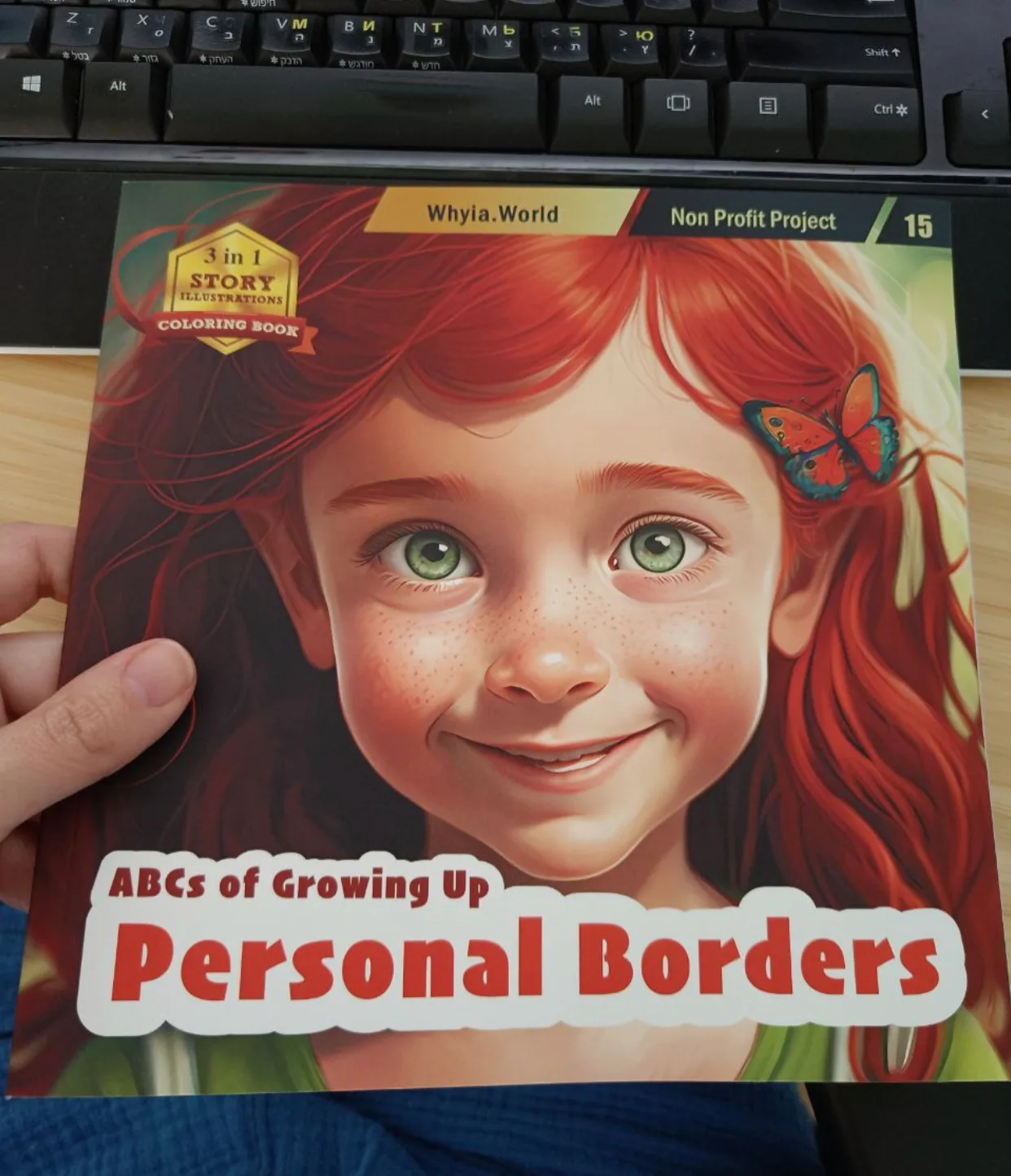 A hand holds a copy of Personal Borders, book 15 in the ABCs of Growing Up series, with a smiling red-haired girl drawn on the cover
