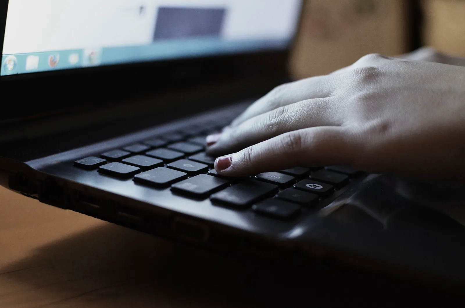 A hand resting on the keyboard of a black laptop, the screen glowing out of focus above it