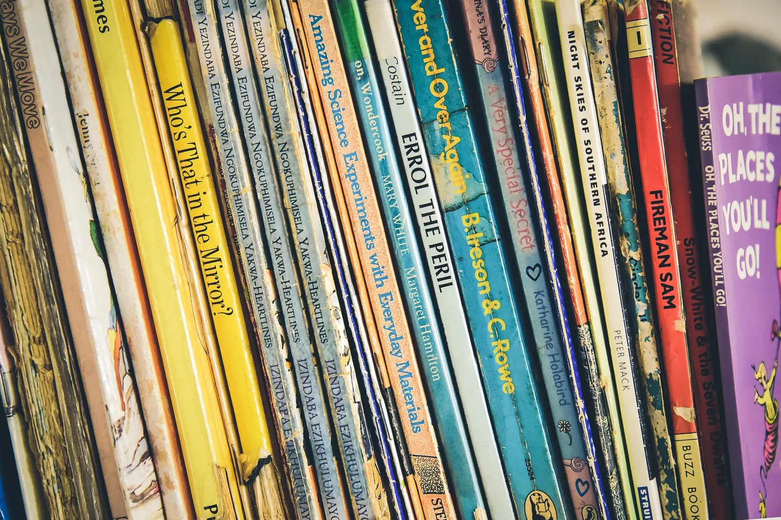 Worn paperback children's books packed tightly on a shelf, their spines showing titles such as Oh, the Places You'll Go! and Fireman Sam