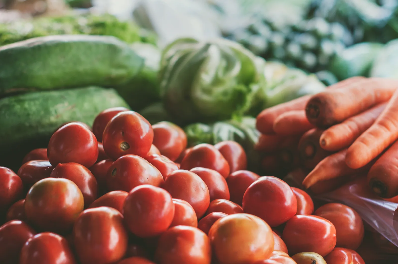 A heap of red tomatoes in front of carrots and green vegetables