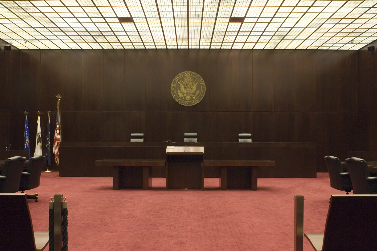 An empty wood-paneled courtroom with a red carpet, three chairs behind the judges' bench, a lectern, flags on the left and a round seal on the wall reading United States Court of Appeals, Seventh Circuit