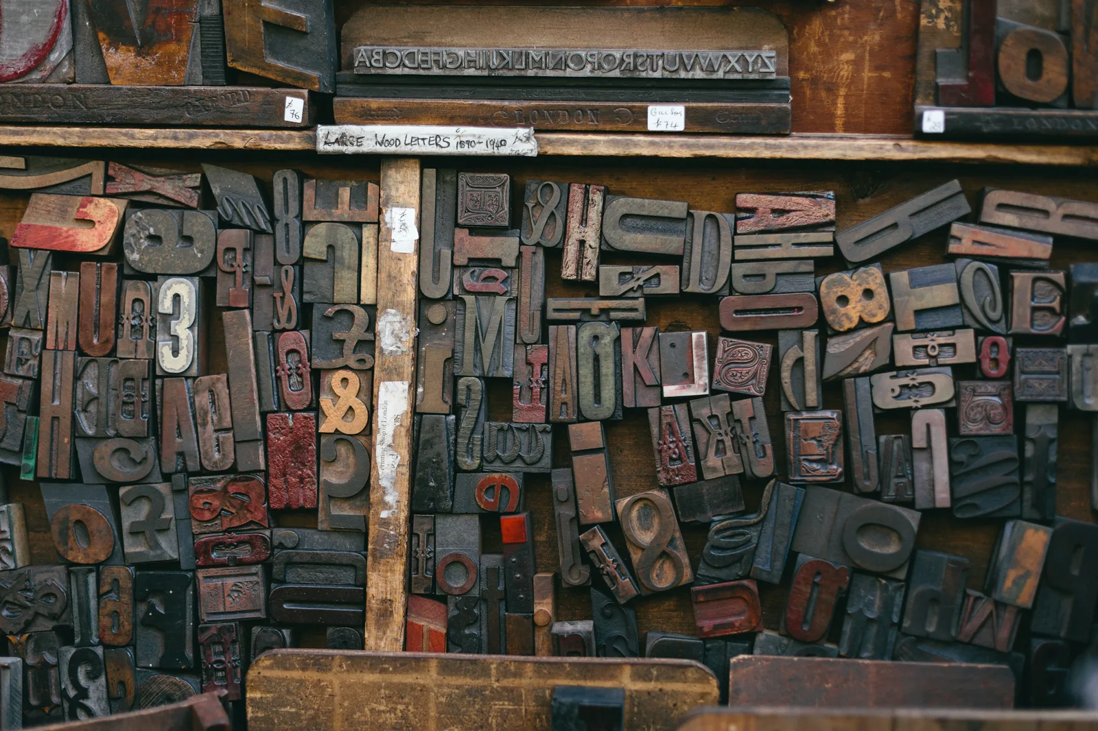 Shelves crowded with old wooden printing letters of many sizes and colors, under a handwritten label for large wood letters