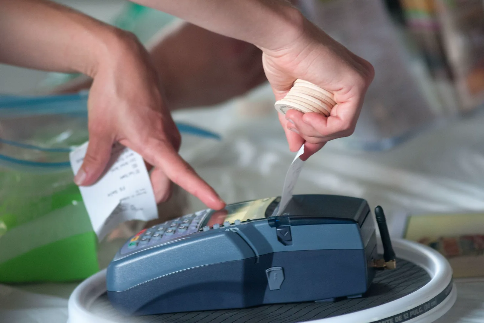 Hands holding a receipt and a stack of wooden tokens over a portable card reader on a market table