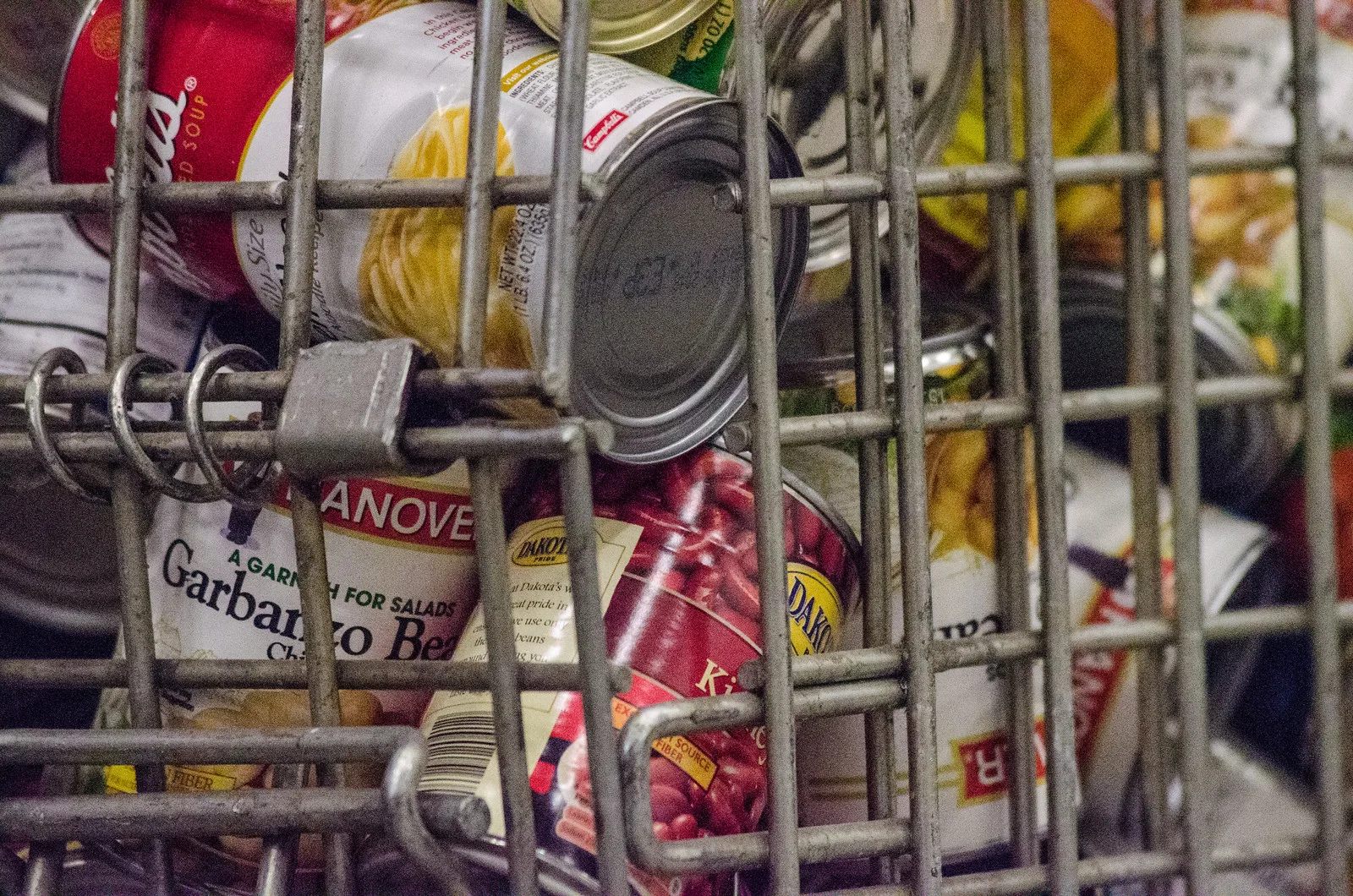 Cans of soup, garbanzo beans and kidney beans piled behind the bars of a metal wire bin